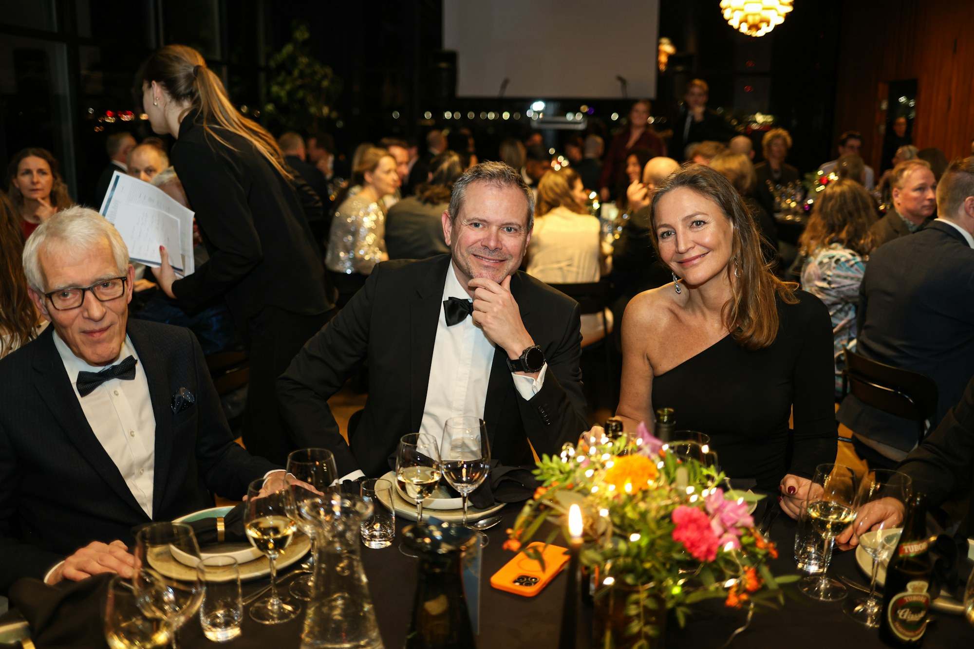 Guests in black tie smiling at a candlelit charity gala dinner