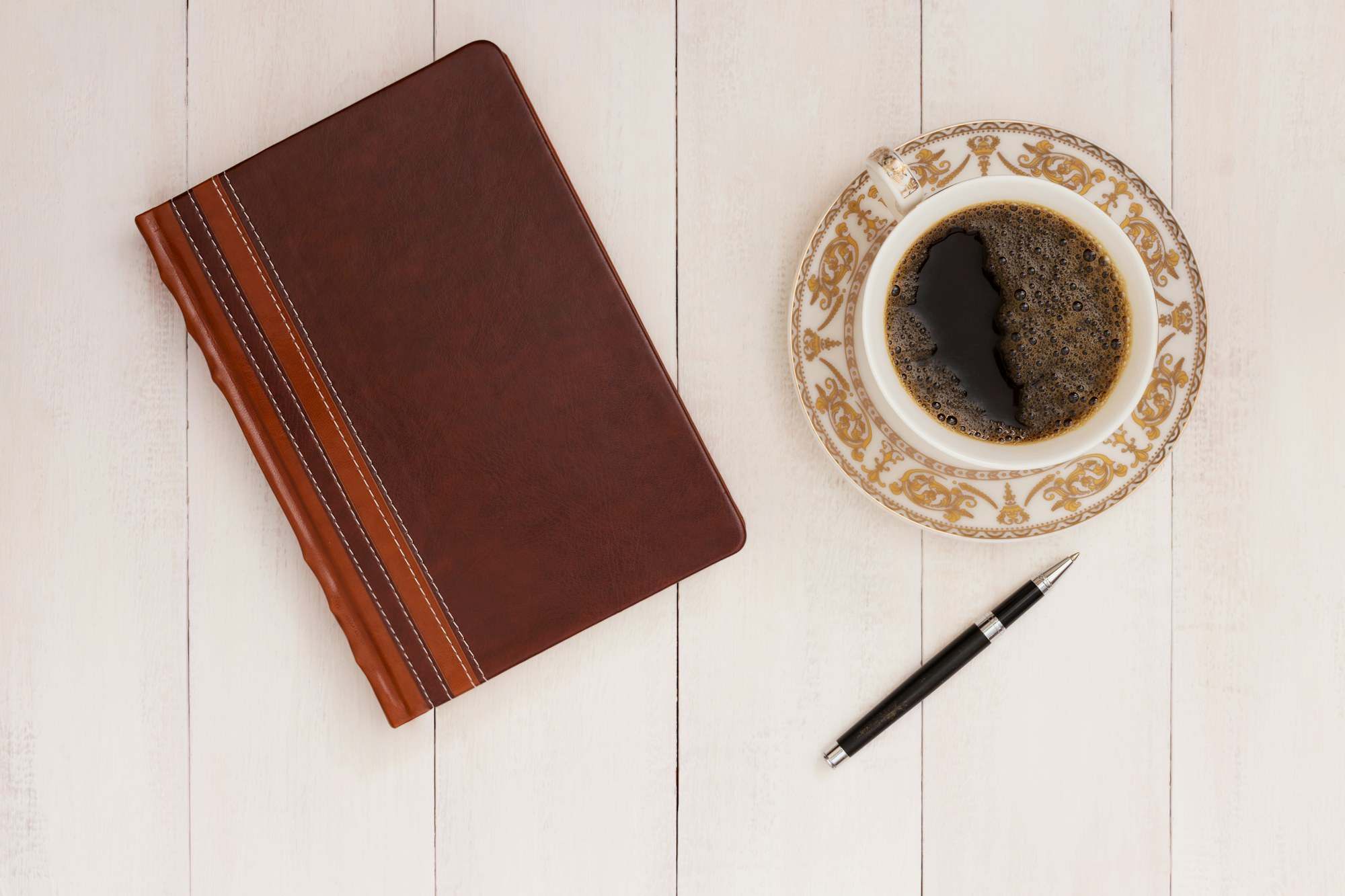 Notebook, pen and a cup of coffee on a white table