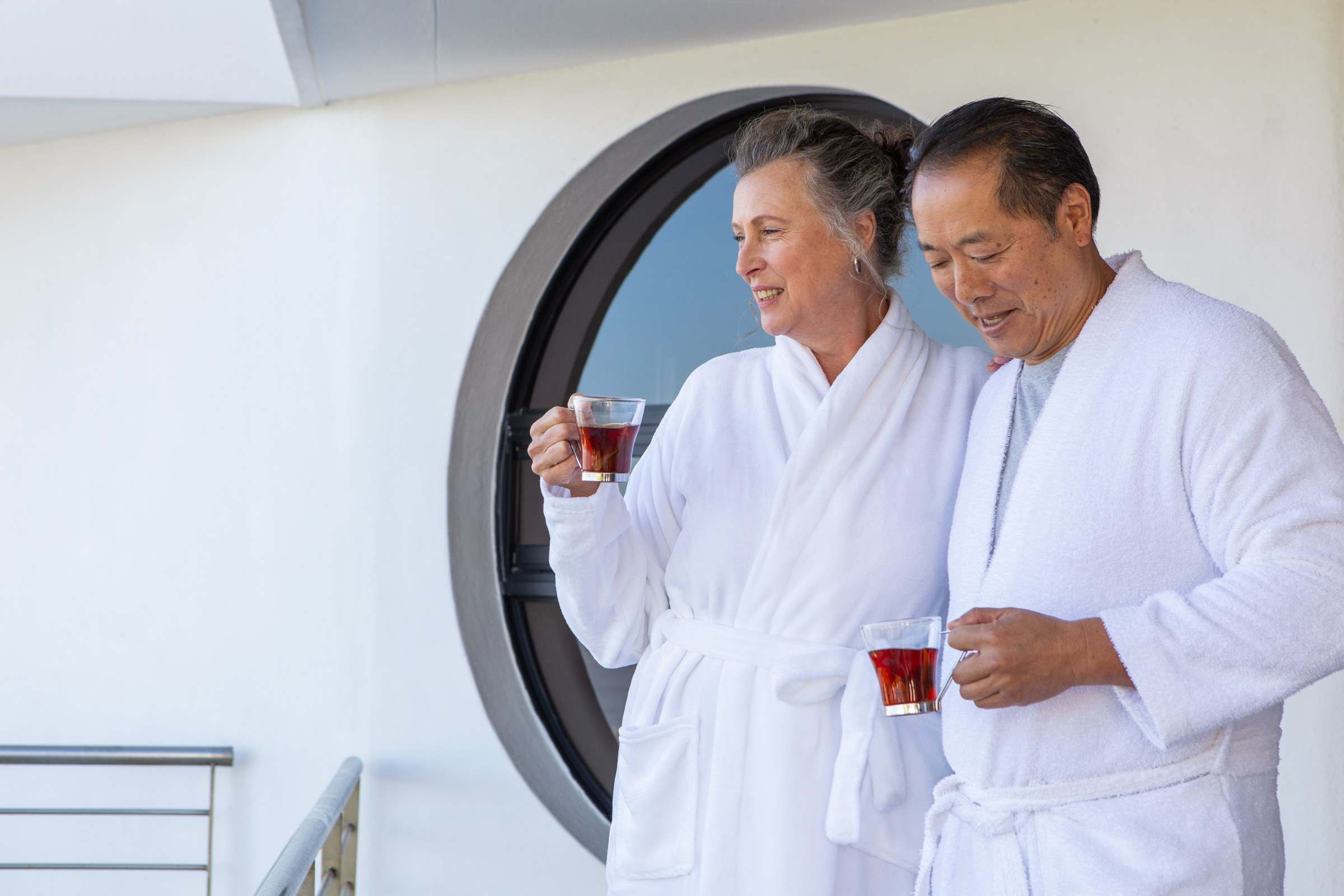 Older couple in white robes sharing tea on a cruise ship balcony