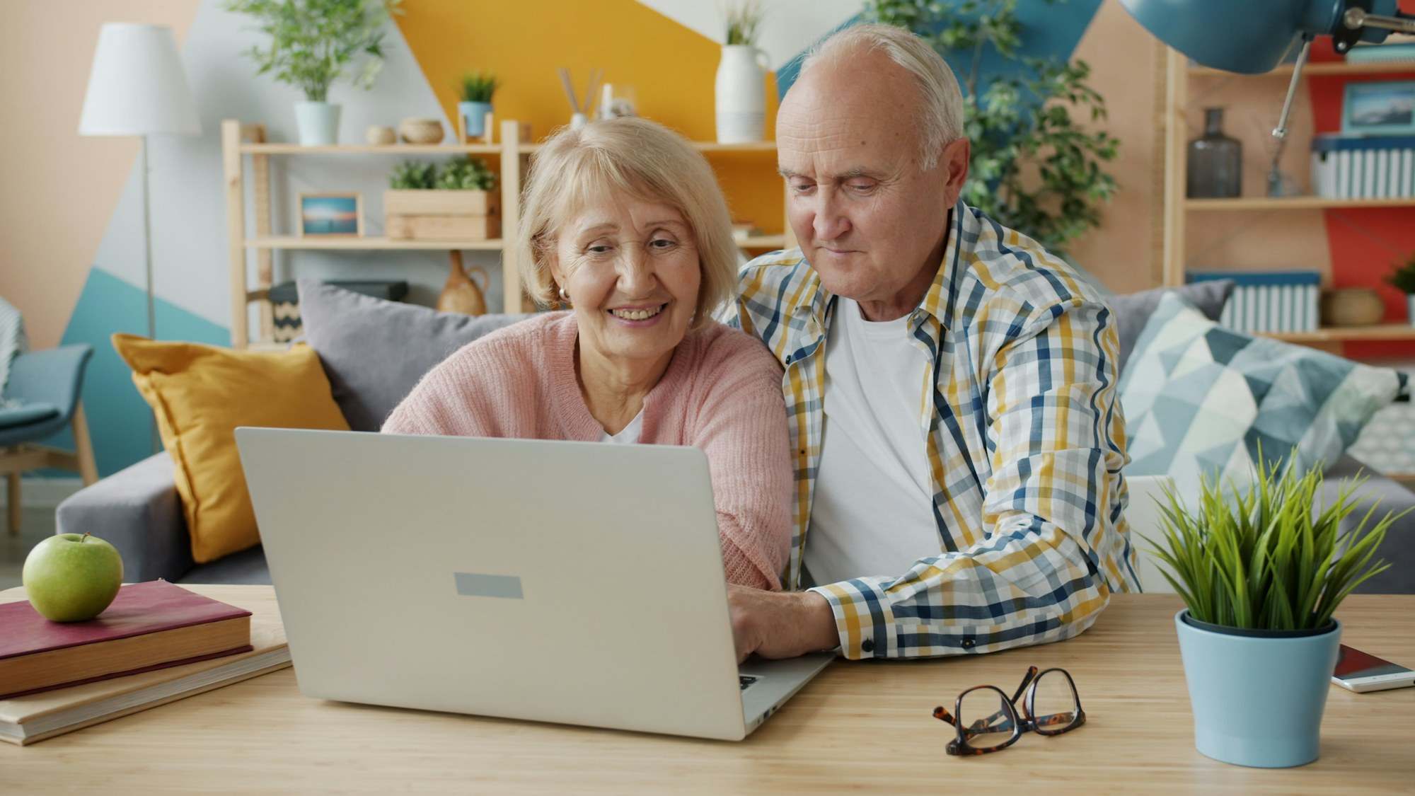 Older couple smiling at a laptop on a video call from their living room