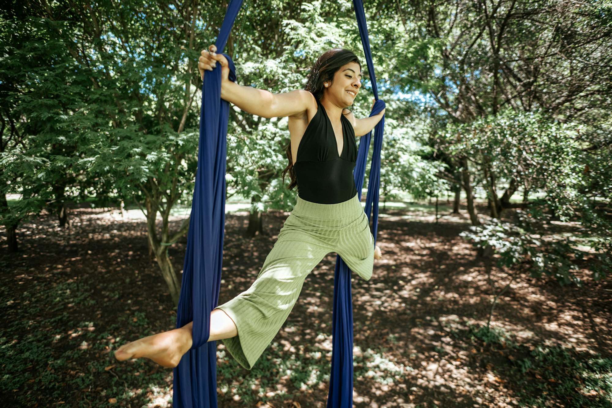 Woman practicing aerial yoga on silks in a leafy garden