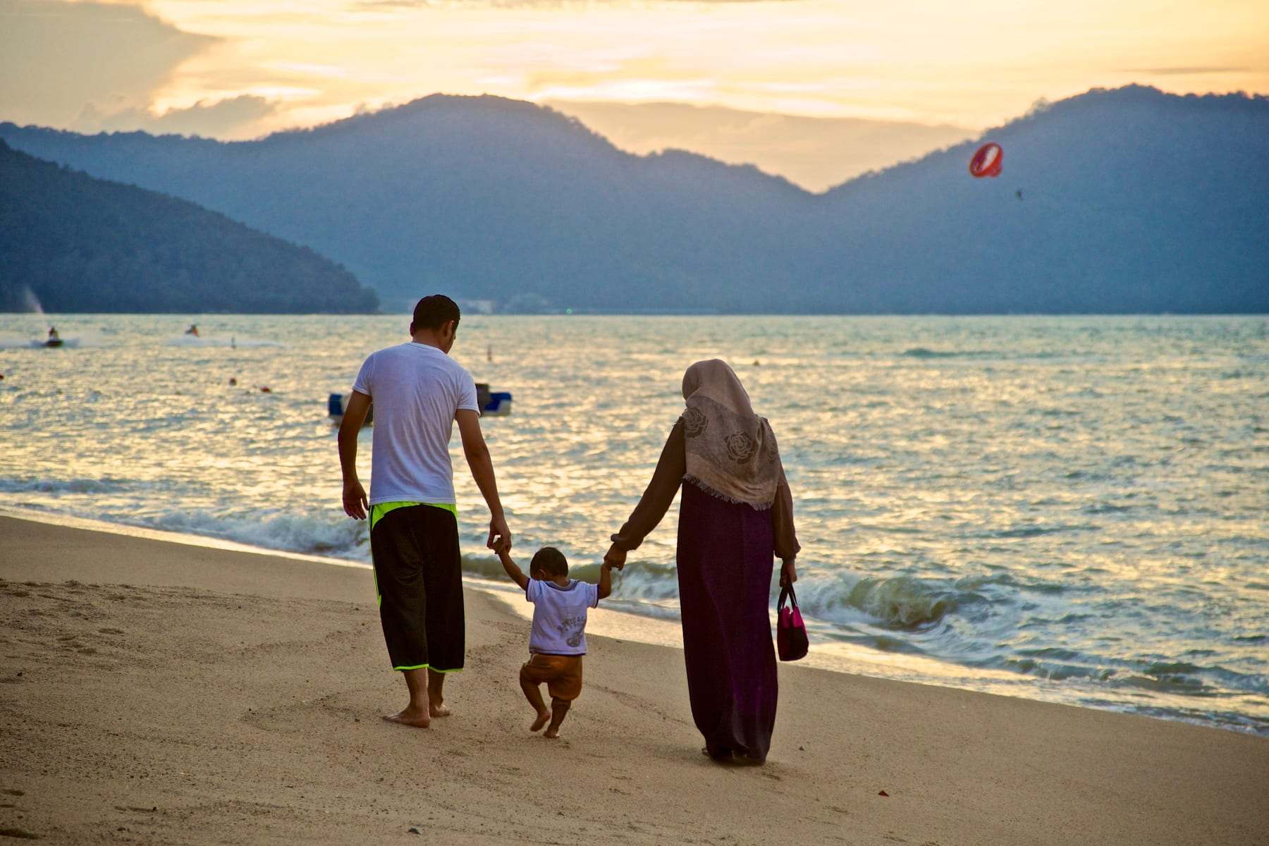 Parents walking a toddler along a beach at sunset
