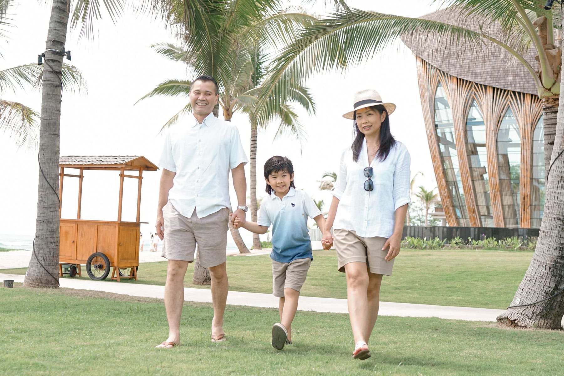 Parents walking hand in hand with their young son through a resort garden