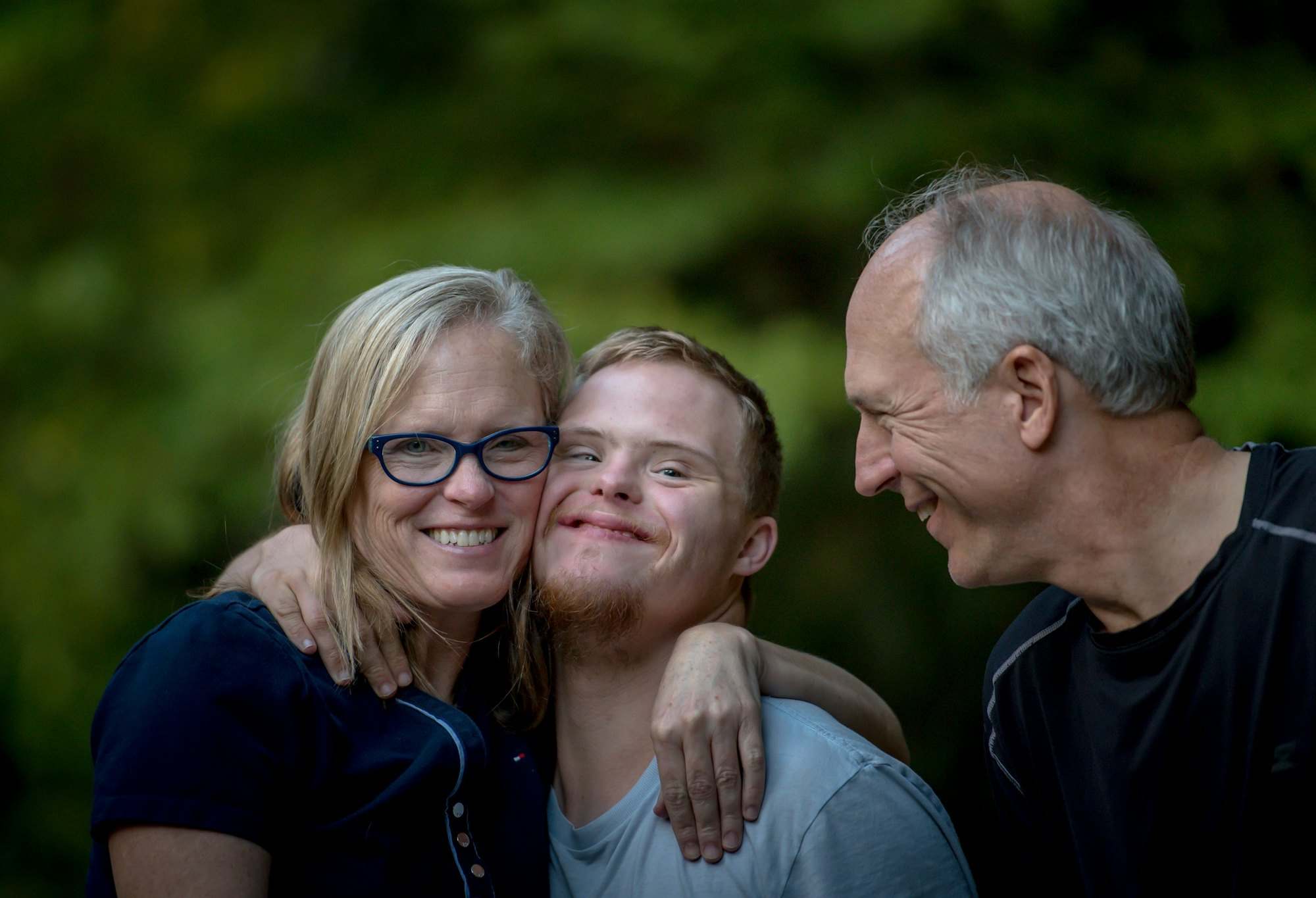 Mother, father and their adult son with Down syndrome smiling together outdoors